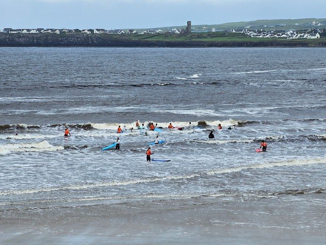 A class of beginner surfers in waist high water as waves break around them